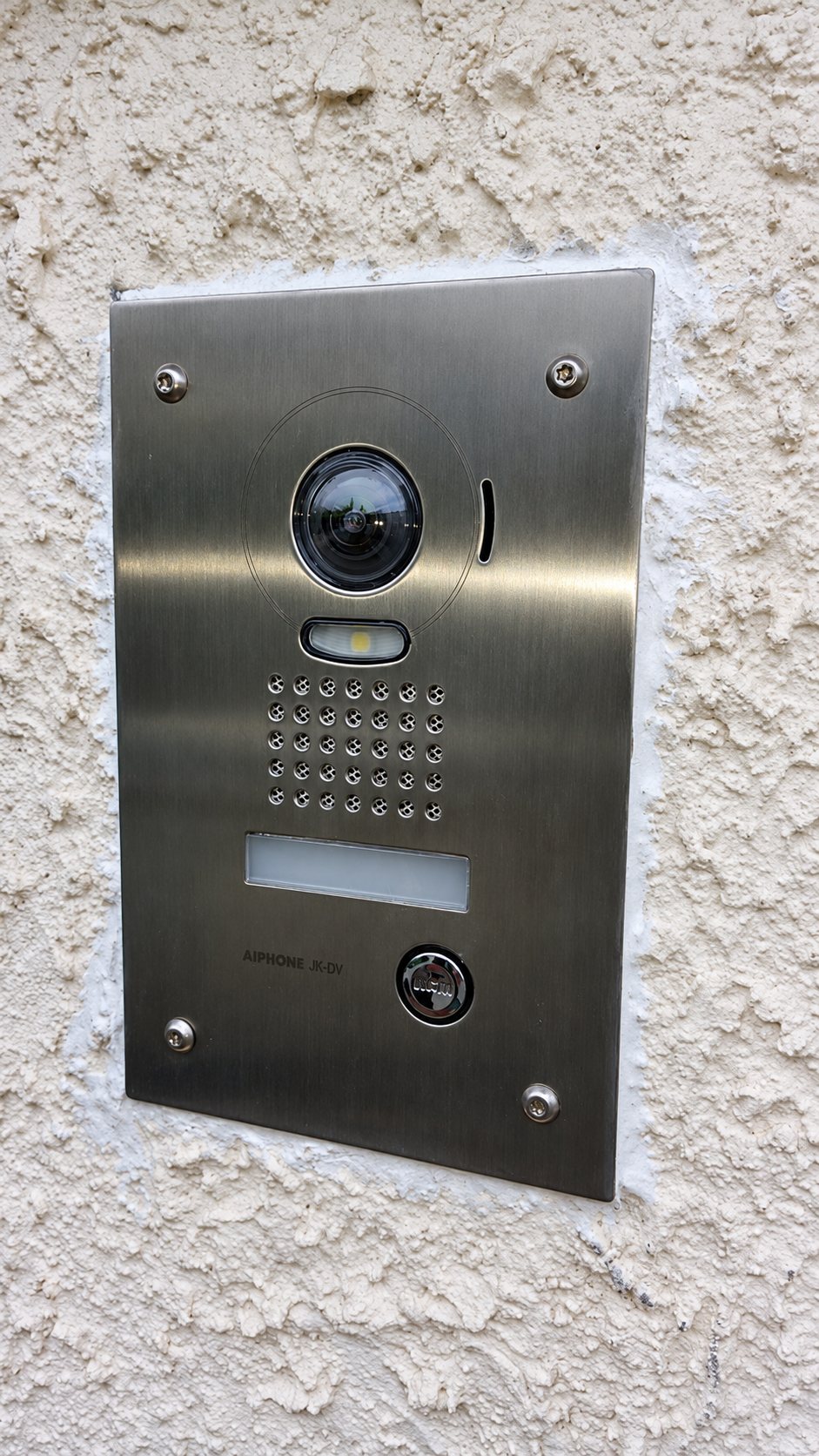 Portier vidéo en inox encastré dans un mur crépi blanc