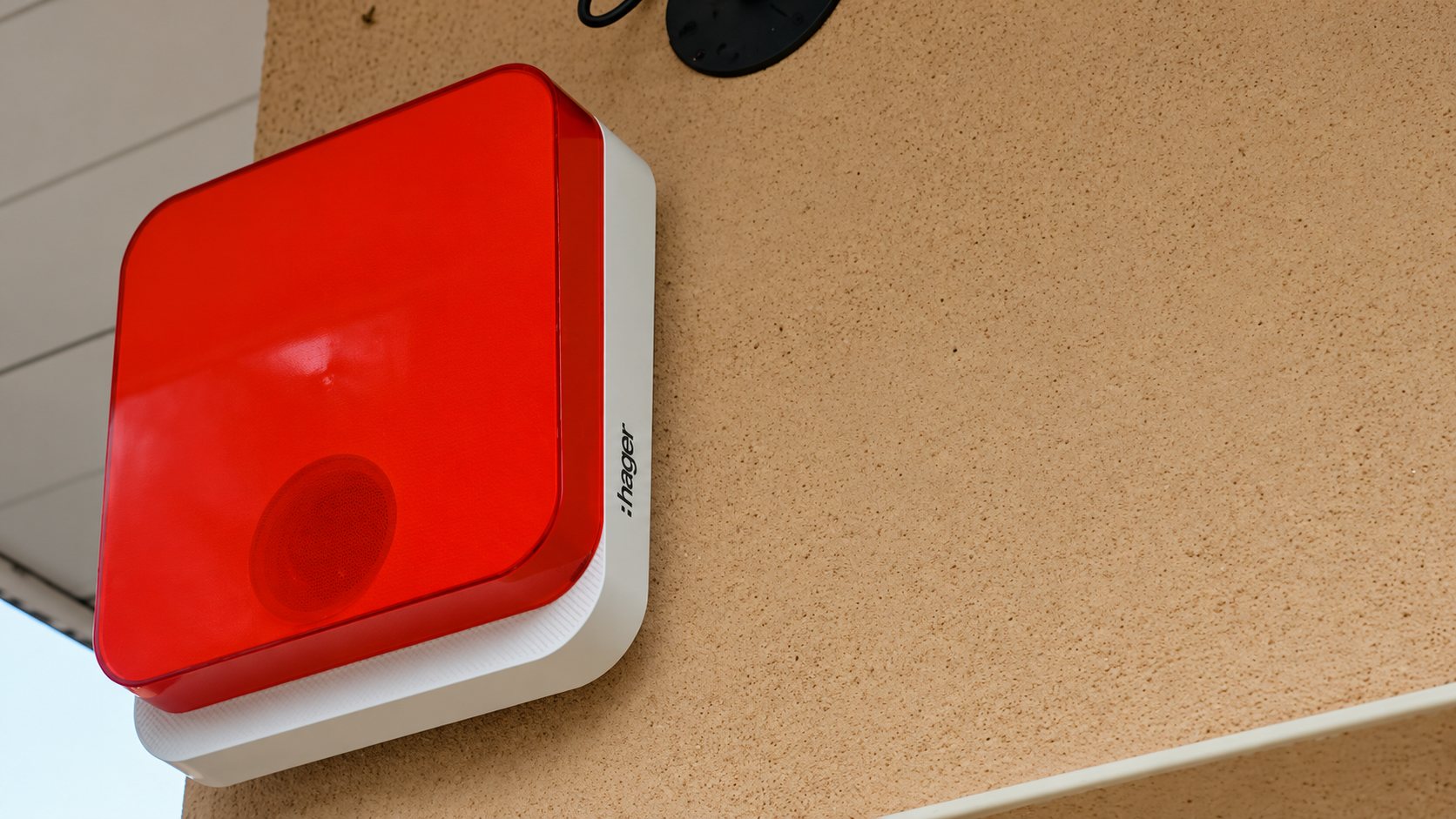 Sirène d'alarme extérieure rouge et blanche fixée sur un mur crépi